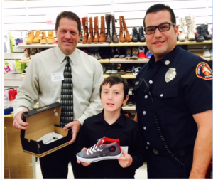 HOLIDAY SPIRIT – Rotary Club of La Mirada President John Lewis (l) and Los Angeles County Fire Department Captain Hugo Valdivia from Fire Station 15 assist a local child select new shoes during the Rotary Club of La Mirada’s annual Holiday Shopping Spree at Marshalls.